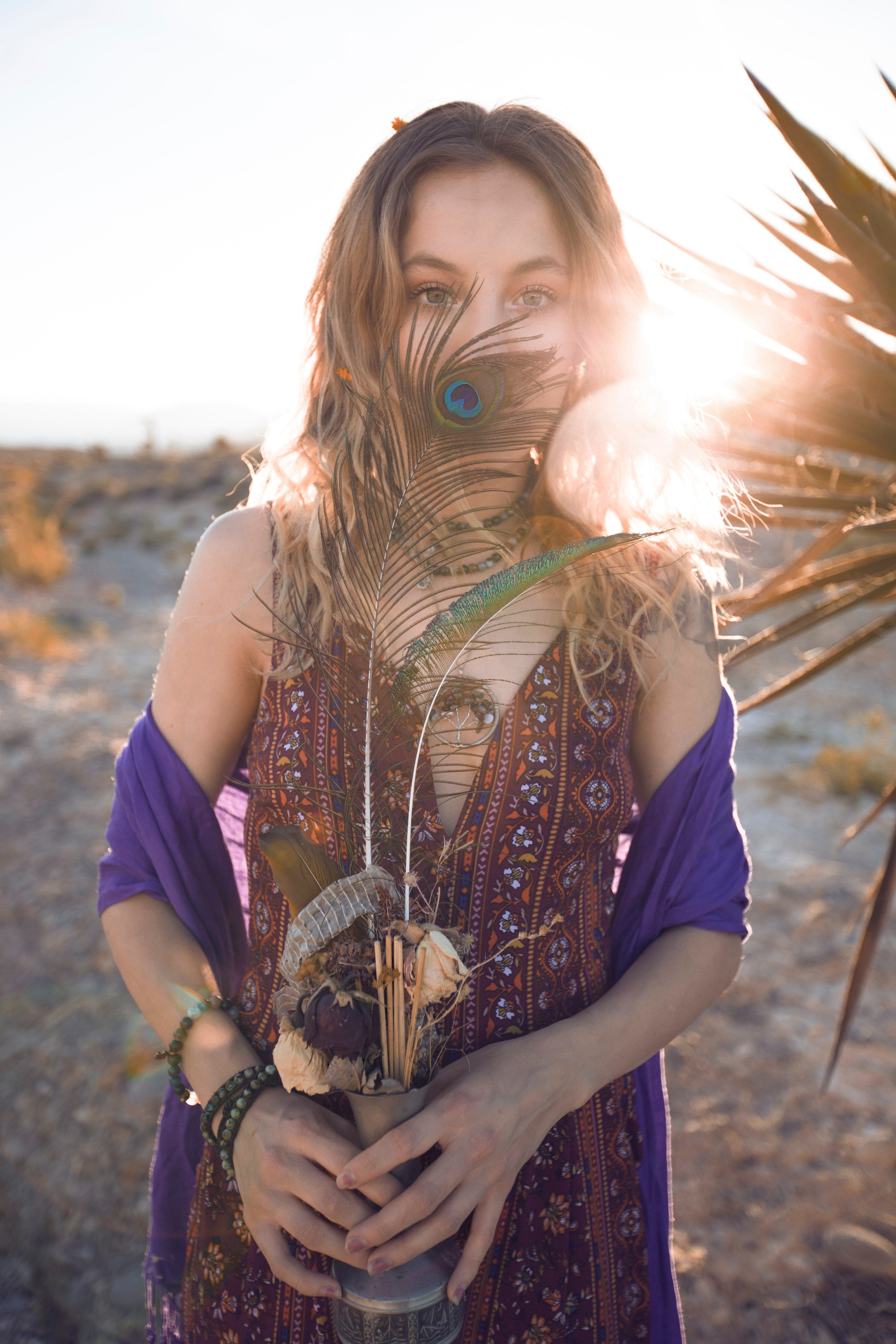 Woman dressed in new age clothes holds a peacock feather to her face