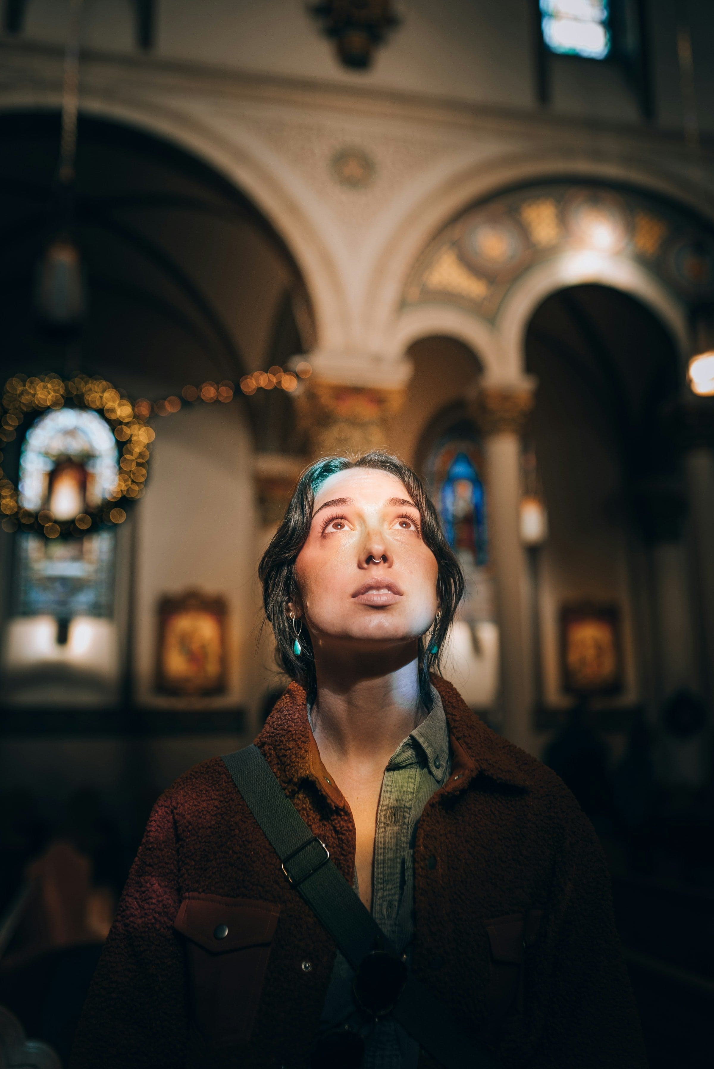 Woman standing in church. Light is on her face as she looks upwards, terrified or in awe.
Photo by Josh Hild on Unsplash